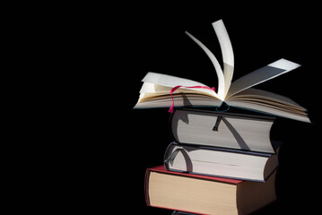 A stack of books against a dark background. The top book is open and the pages are blowing around....