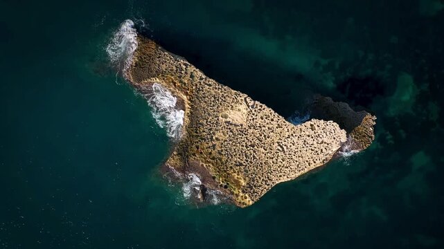 Abstract top-down aerial view of a unique rocky penisula in the deep blue ocea.