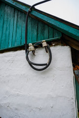 White plastered building wall with green wooden roof and black corrugated cables