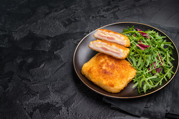 Chicken cordon bleu cutlet with cheese and ham on plate with salad. black background. top view
