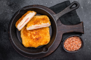 Fried cordon bleu cutlet with cheese and ham in pan. black background. top view