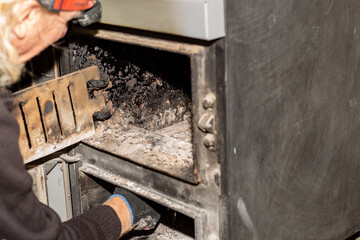 A gloved hand reaches inside a wood burning stove of a fuel boiler, cleaning its parts