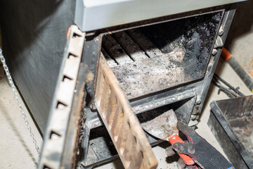 A gloved hand uses a tool to clean the inside of a dirty solid fuel heater stove
