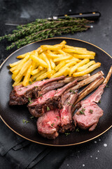 Roast lamb cutlets, mutton meat steaks on plate with french fries. black background. top view