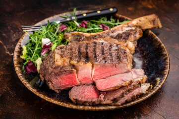 Grilled and sliced Tomahawk beef steak, marble  rib eye with bone on plate with salad. brown background. top view