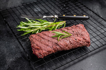 Grilled Flank steak, beef meat on rack with rosemary. black background. top view