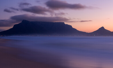 Long exposure of Table Mountain silhouette at colourful sunset from Sunset Beach, South Africa