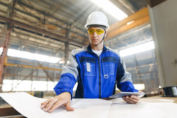 Male industrial engineers use computer for control at project with blueprints in industry factory...