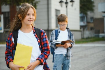 Little schoolgirl with backpack and books near school