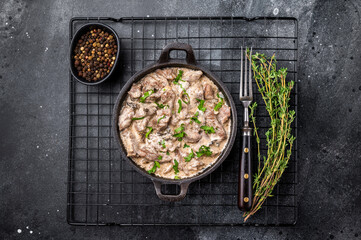 Creamy beef stroganoff with fresh greenery in a skillet. black background. top view
