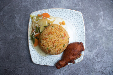 Golden brown fried chicken, flavorful fried rice and mixed vegetables in plate on a rustic wooden table top view of main course