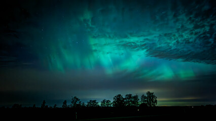 Naklejka premium Northern lights dancing behinde the dark clouds over country landscape