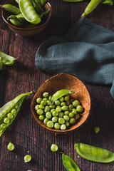 Bowl with green sugar peas on wooden table vertical view