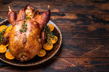 Roast goose with apples and oranges on plate with herbs. wooden background. top view