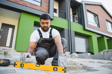 Indian Worker skillfully laying paving stones using a hammer and wearing gloves, showcasing...