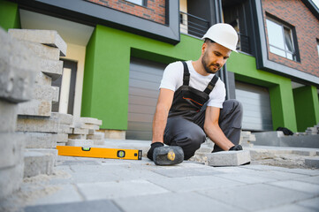 The master in gloves lays paving stones in layers. Garden brick pathway paving by professional...