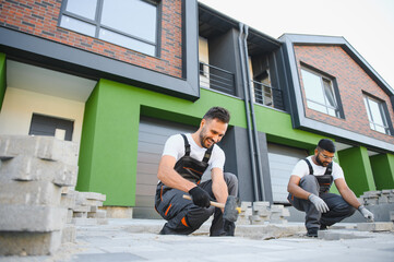 A group of multiracial workers lay paving stones on a sidewalk near a house