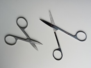 Two pairs of stainless steel scissors on a light surface. One pair of scissors is closed and the...