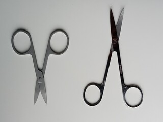 Two pairs of stainless steel scissors on a light surface. One pair of scissors is closed and the...
