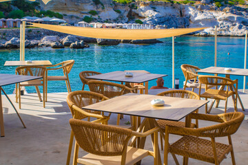 Cafe chairs and tables, Kalithea Springs beach in the background, Rhodes, Greece