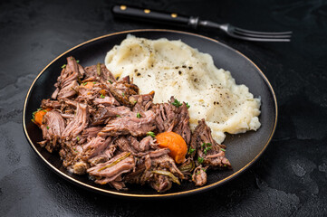 Beef stew with mashed potatoes, carrots and herbs on a plate isolated. black background. top view
