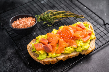 Toast with salty salmon, trout slices, avocado and red caviar. black background. top view