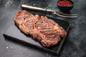 Roasted Chuck eye roll steak, marbled beef meat on a board. black background. top view