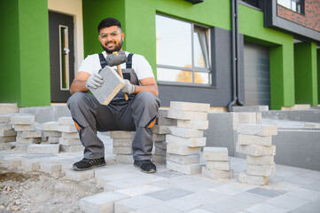 Indian master in gloves lays paving stones in layers. Garden brick pathway paving by professional...