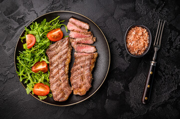 Grilled Steak from Black Angus beef meat on a plate with salad. black background. top view