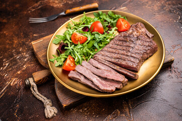 Roast dry aged Top Sirloin beef steak on plate with salad. brown background. top view