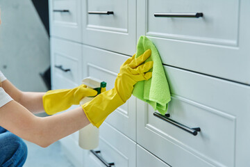 Close up hands in gloves cleaning kitchen, washing facade of kitchen furniture