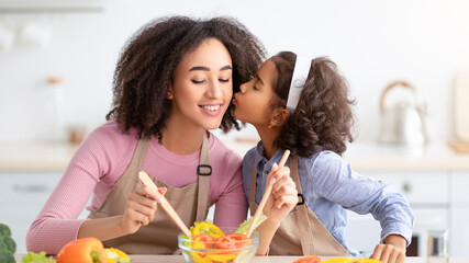 Happy Loving Family. Portrait of smiling african american woman cooking tasty meal, mixing salad in...