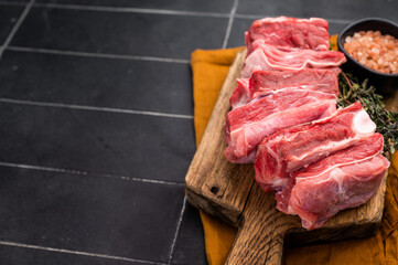 Fresh lamb rack rib pieces, mutton meat with thyme on wooden board. black background. top view