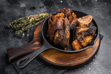 Tender beef short ribs in a pan, seasoned with herbs and spices. Perfect for culinary blogs or restaurant menus that focus on hearty, flavorful meat dishes. black background. top view