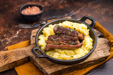 Close-up of tender beef short ribs, beautifully caramelized and resting on a bed of creamy mashed potatoes, creating an inviting culinary scene. brown background. top view