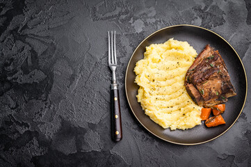 Braised beef short ribs resting on a bed of creamy mashed potatoes, creating an inviting culinary scene. black background. top view