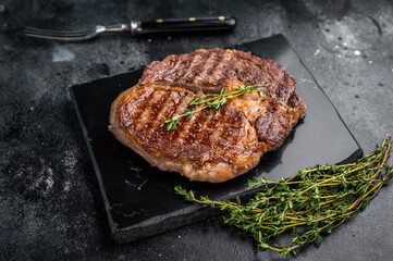 Rib eye steak with herbs on marble board, grilled prime beef meat. black background. top view