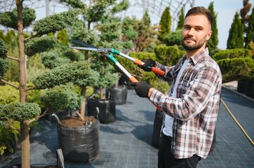 A young gardener cuts a tree with scissors. Gardening and tree shop concept