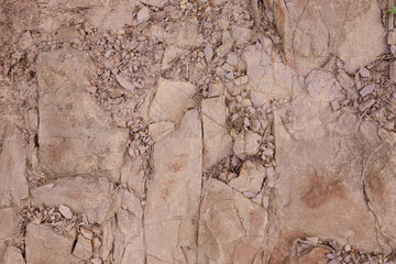 Brown rock texture with a rough, uneven surface and small stones. Ideal for use in architecture, design, construction, ecology, and education