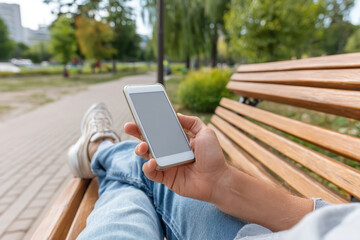 Person relaxing on bench using smartphone in park during sunny day