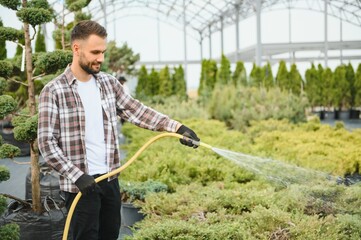 Young male gardener watering plants with a shower head and hose