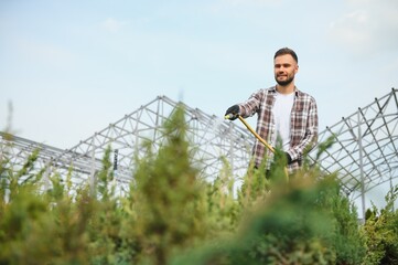 Young male gardener watering plants with a shower head and hose