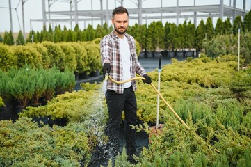Young male gardener watering plants with a shower head and hose