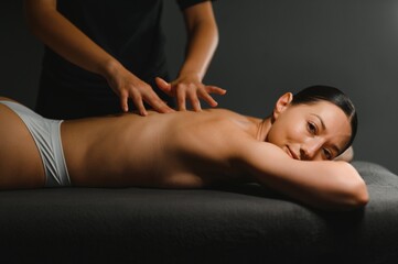 Closeup of relaxed young woman lying face down on massage table and enjoying remedial body massage...