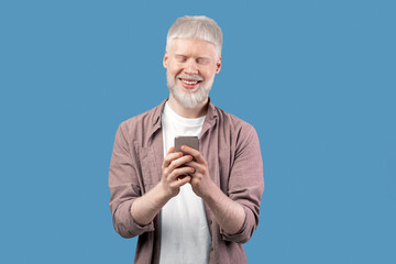 Online life. Happy albino man using smartphone over turquoise studio background. Bearded excited guy chatting online, browsing social media. People and technology concept