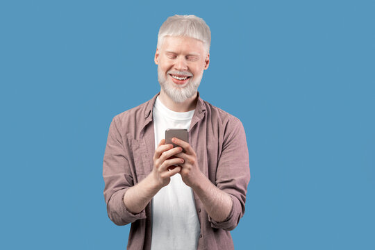 Online life. Happy albino man using smartphone over turquoise studio background. Bearded excited guy chatting online, browsing social media. People and technology concept - Powered by Adobe