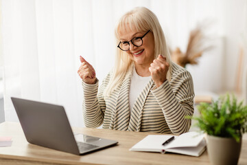 Win Concept. Portrait of excited mature woman in eyeglasses celebrating success shaking clenched...