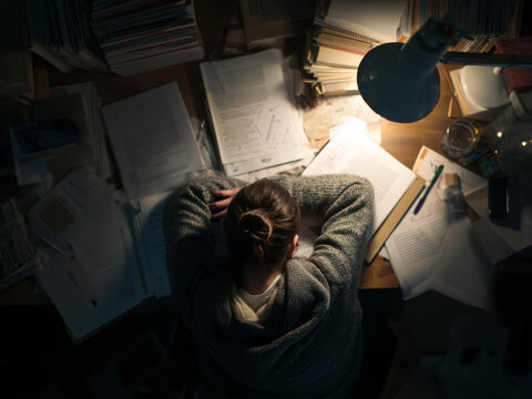 Top view of student asleep at desk while studying, books and notebooks scattered, cozy lighting, photorealistic, no visible face or hands
