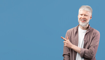 Cool offer. Confident albino man pointing at free space on turquoise studio background. Guy with...