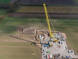 Large heavy-duty crane sets first parts for the tower of a wind turbine, building construction,...